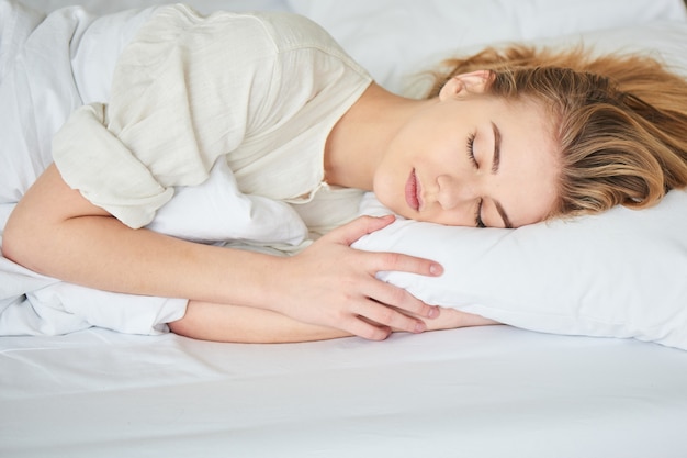 A menina loira está dormindo na cama branca