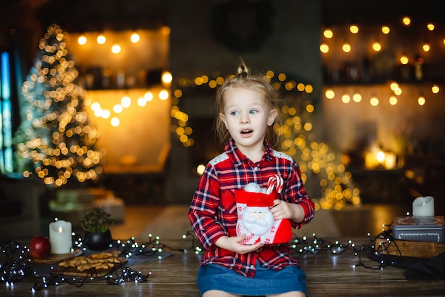 A menina loura bonito da criança em uma camisa vermelha quadriculado obtém um presente do Natal.