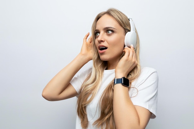 A menina loura nos fones de ouvido gosta de música em um fundo branco