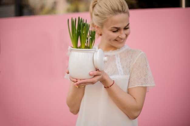 A menina loura prende a planta no vaso de flores