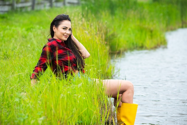 A menina morena está se divertindo no rio com botas de borracha no país Jovem mulher em um lago aproveita a vida