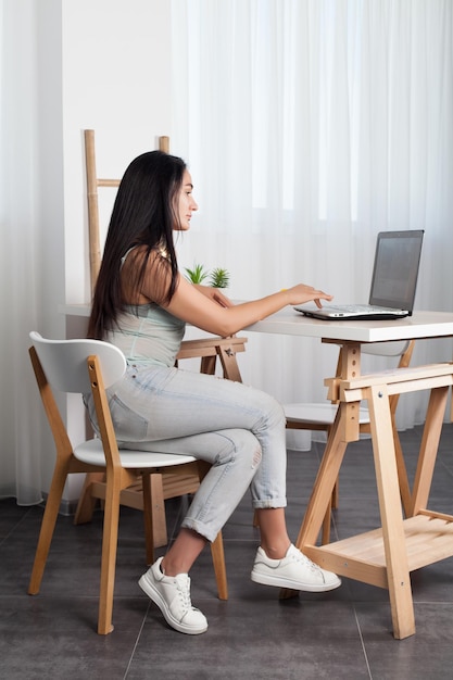 A menina morena se senta na mesa e trabalha com notebook