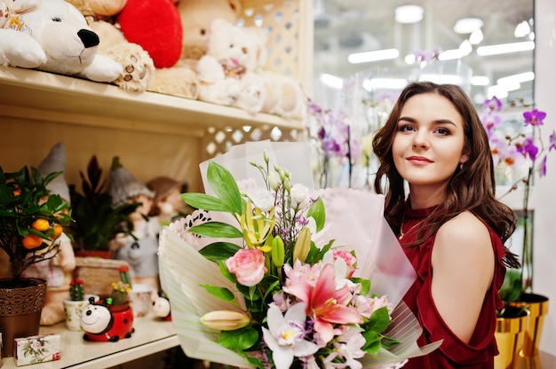 A menina moreno na compra vermelha floresce na loja de flor.