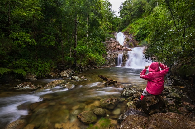 A menina na camisola vermelha que visita na cachoeira do Pi-tu-gro, cachoeira bonita na província de Tak, ThaiLand.