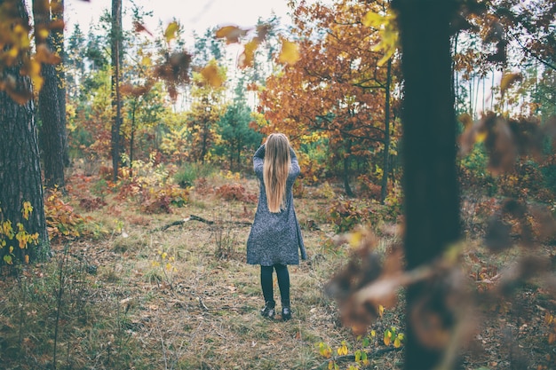 A menina na floresta do outono tem um cabelo branco longo e saudável,