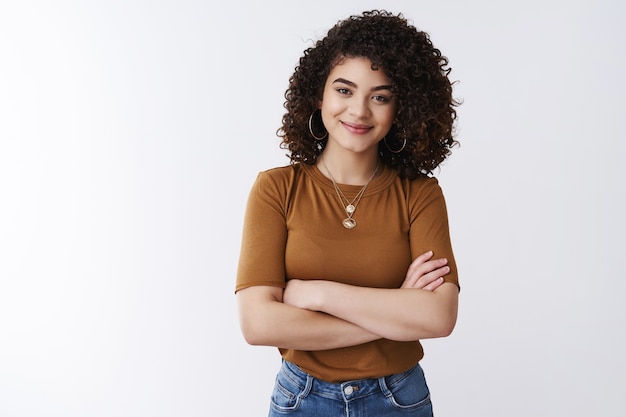 A menina não tem medo de tarefas desafiadoras. bem-sucedida, feliz, confiante, bonita, cabelos cacheados, gerente de atendimento ao cliente, mulher, braços cruzados, sorriso, tórax, assertiva, autoconfiante, sentir-se fortalecida, relaxada