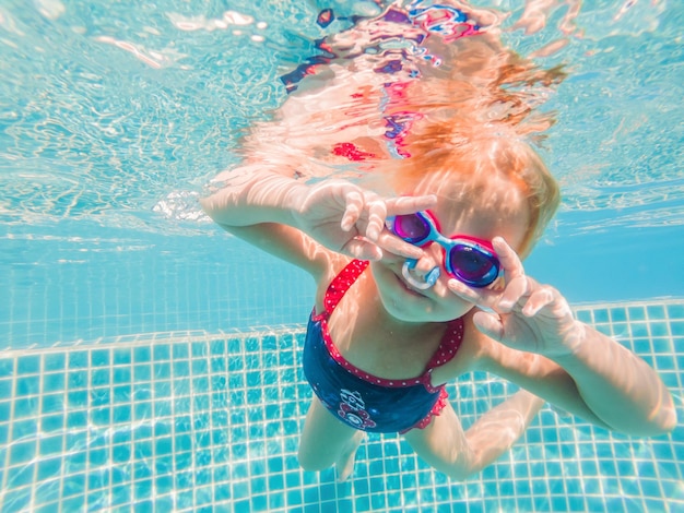 A menina no parque aquático nadando debaixo d'água e sorrindo