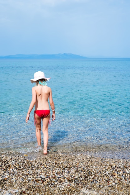 A menina no roupa de banho e no chapéu branco olha o mar.