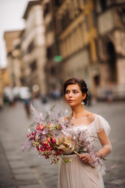 A menina-noiva está com um belo padrão de flores como uma máscara em Florença, noiva elegante em um vestido de noiva em pé com uma máscara na cidade velha de Florença. Garota modelo em Florença.