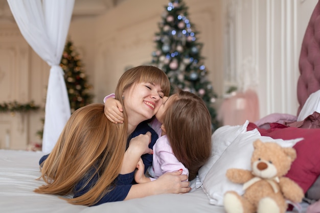 A menina passa o tempo brincando com a mãe enquanto está deitada na cama. Conto de Natal. Infância feliz.