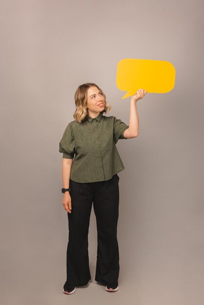 A menina pensativa está segurando um balão de fala enquanto ela está olhando para ele sobre a parede cinza