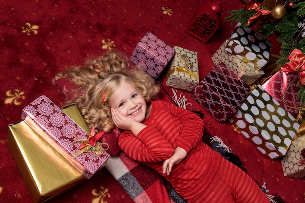 A menina pequena feliz no vestido com tem um presente de natal