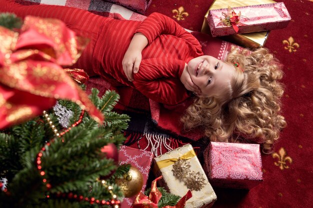 A menina pequena feliz no vestido com tem um presente de Natal