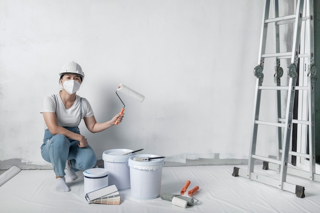 Foto a menina pinta uma parede branca com um rolo. reparação do interior.