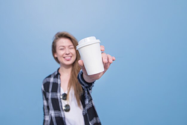 A menina positiva mostra um vidro branco com café em um fundo gooed. Concentre-se no vidro. Café com você