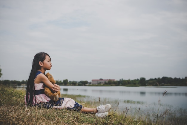 A menina que senta-se com seu urso virou-se no campo dos prados.