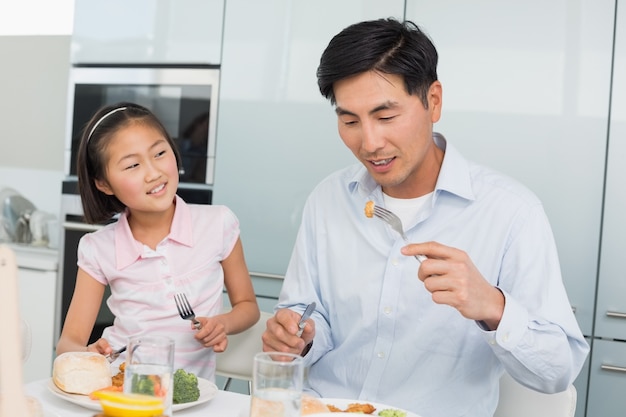 A menina que vê o pai come comida com um garfo na cozinha