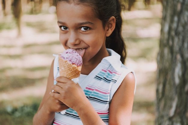 A menina satisfeita nova come o gelado na floresta.