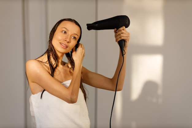 Foto a menina seca o cabelo com um secador de cabelo jovem no banheiro