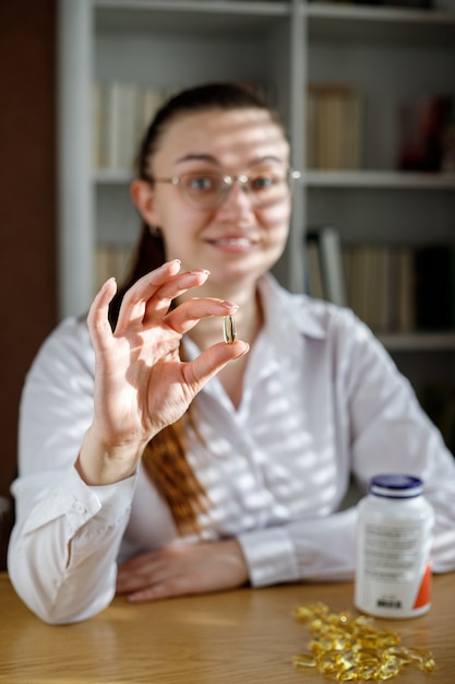 A menina segura uma cápsula de óleo de peixe na mão. Cápsulas de Omega3 na mesa e na mão do médico