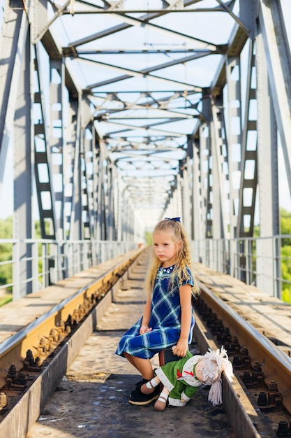 A menina senta em uma mala em uma plataforma sobre trilhos Faltando tristeza longe de casa