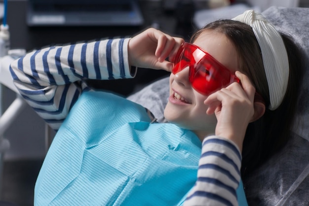 A menina senta-se na cadeira odontológica e usa óculos de proteção Ela brinca