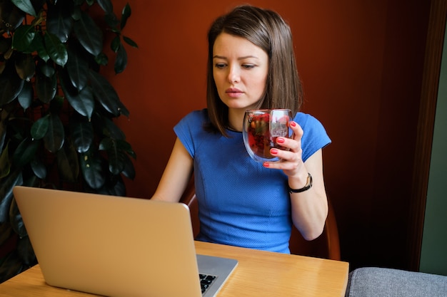 A menina senta-se no café e trabalha no laptop e bebe chá.