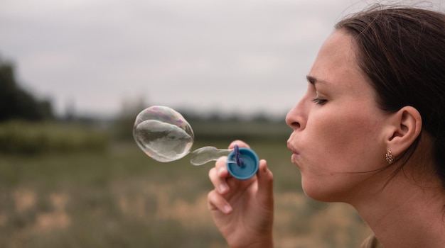 A menina sopra bolhas de sabão Uma jovem senta-se na natureza e sopra bolas de sabão Rosto no perfil