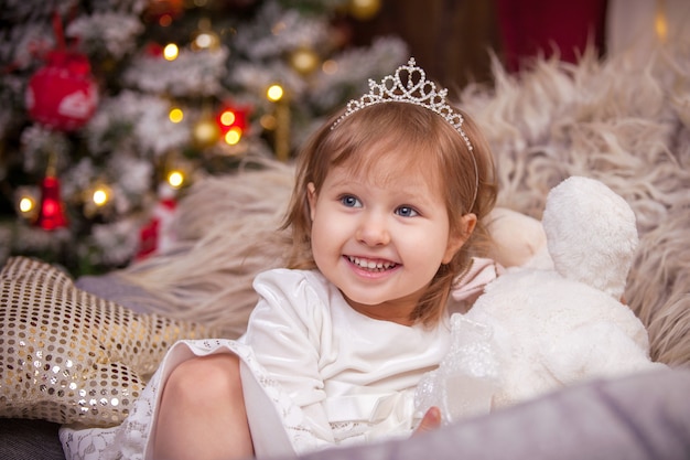 A menina sorri, uma árvore de Natal nas luzes e uma janela com uma guirlanda envolvem a atmosfera do feriado