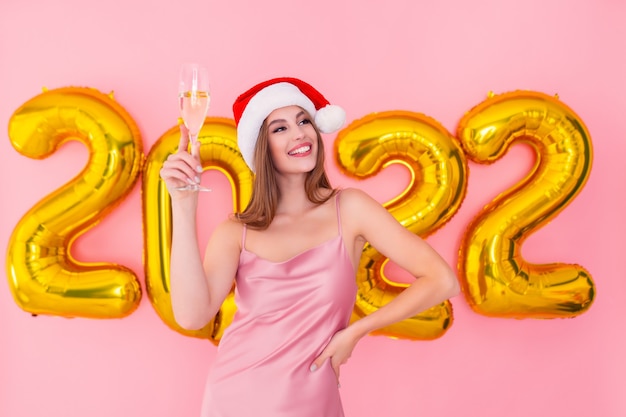 A menina sorridente do papai noel levanta uma taça de champanhe com números dourados e balões de ar no conceito de ano novo