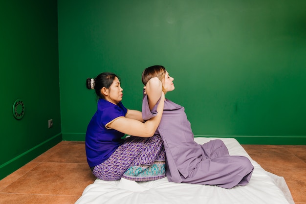 A menina tailandesa nova do trabalhador do massagista no traje exótico asiático étnico faz e demonstra procedimentos diferentes dos termas tradicionais na sala verde da ioga do relaxamento