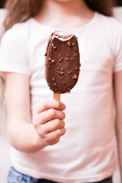 A menina tem na mão um picolé mordido em cobertura de chocolate com nozes