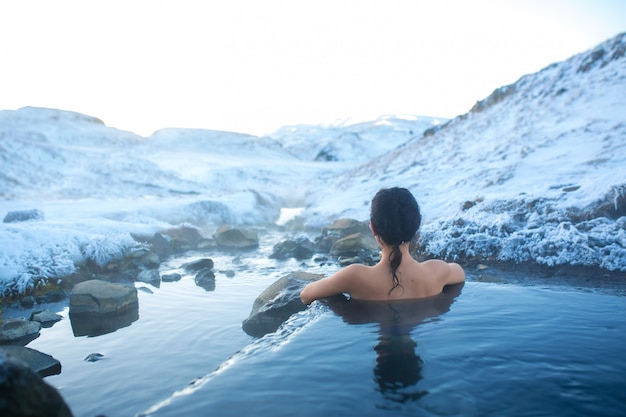 A menina toma banho em uma primavera quente ao ar livre com uma vista deslumbrante das montanhas nevadas. islândia incrível no inverno