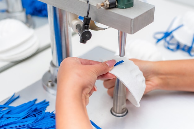 A menina trabalha em uma fábrica para a produção de máscaras médicas com nanofibras e laços de solda com ultra-som em uma máquina.