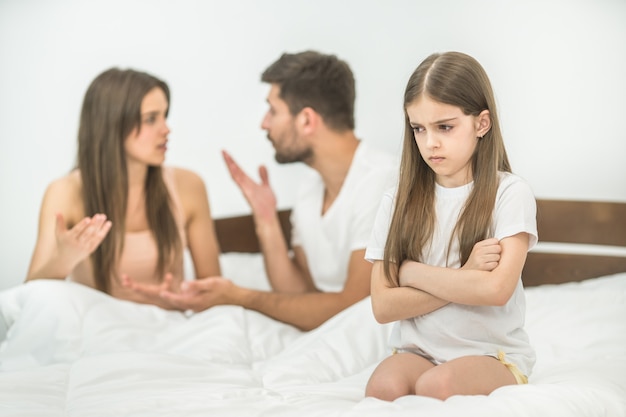 A menina triste sentada perto do gesto dos pais na cama
