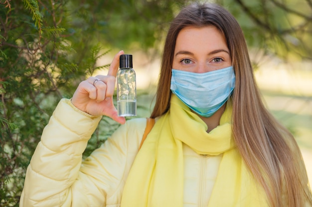 A menina usa uma máscara protetora e segura uma garrafa de gel anti-séptico de álcool, equipamento para desinfecção, pandemia de Covid-19, surto de coronavírus, desinfetante para as mãos para proteger contra doenças contagiosas