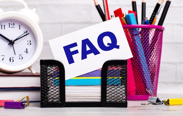 A mesa de escritório tem diários, um despertador e um cartão branco com o texto FAQ Business concept