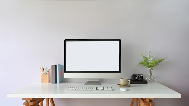 A mesa de trabalho é cercada por um monitor de computador com tela branca em branco e equipamentos de escritório