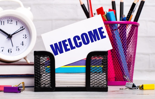 A mesa do escritório tem diários, papel de carta despertador e um cartão branco com o texto WELCOME Business concept