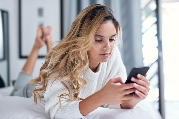 A mídia social me mantém ocupado Foto de uma jovem usando seu celular enquanto estava deitada em sua cama