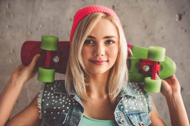 A moça à moda na roupa de brim está guardando um skate.