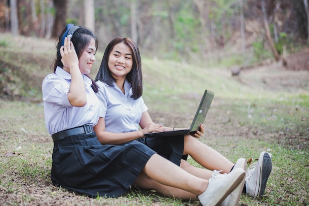 A moça asiática na farda da escola está usando o portátil para a educação e a comunicação no campo de Tailândia.