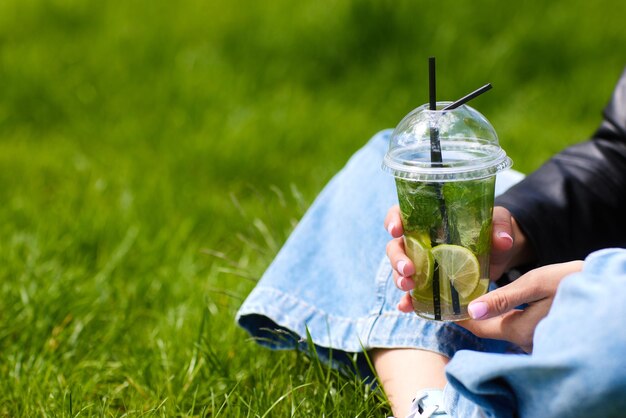 A moça bebe um cocktail refrescante com gelo na grama verde