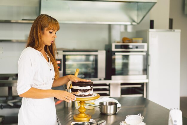 A moça da confeiteira está preparando um biscoito de bolo com creme branco e bolos de chocolate para cozinhar