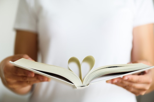 Foto a moça na leitura branca do t-shirt abriu o livro com forma do coração, conceito do amor.