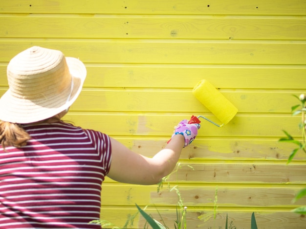 A moça pinta uma parede de madeira com um rolo com tinta amarela