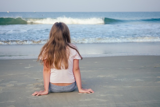 A moça senta-se na areia e olha a água