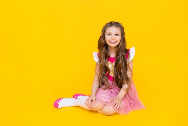 A mocinha está sentada em um fundo amarelo isolado Uma linda garota com cabelos longos em um vestido rosa está sorrindo amplamente