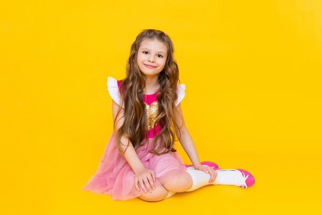 A mocinha está sentada em um fundo amarelo isolado Uma linda garota com cabelos longos em um vestido rosa está sorrindo amplamente