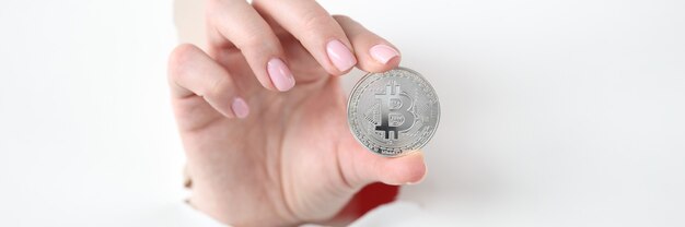 A moeda Bitcoin é segurada à mão através de um orifício no papel branco